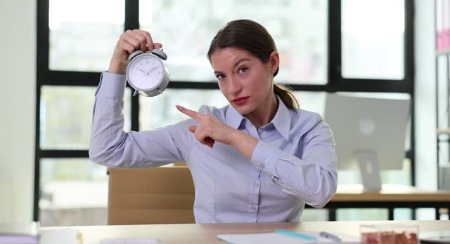 Dissatisfied female boss points finger to clock at workplace