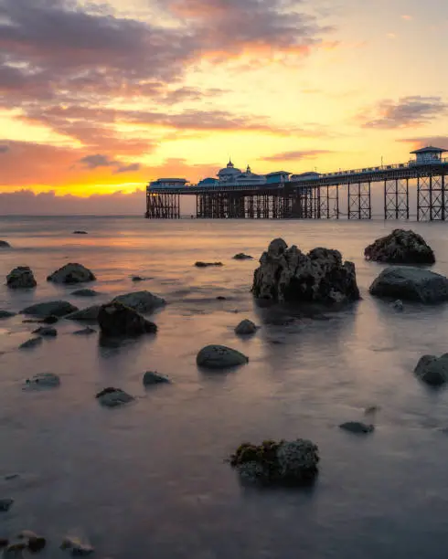 Photo of Vibrant colorful sunrise over the rugged rocky coastline with Llandudno Pier in the background - North Wales