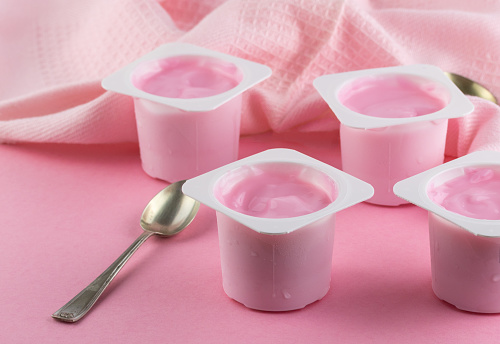Plastic cups with tasty pink yogurt on pink table with silver spoon