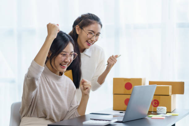 istock Two female Asian small business owners succeed in selling online using laptop computers. Excited happy successful asian business woman raising her hands in joy. 2044488296