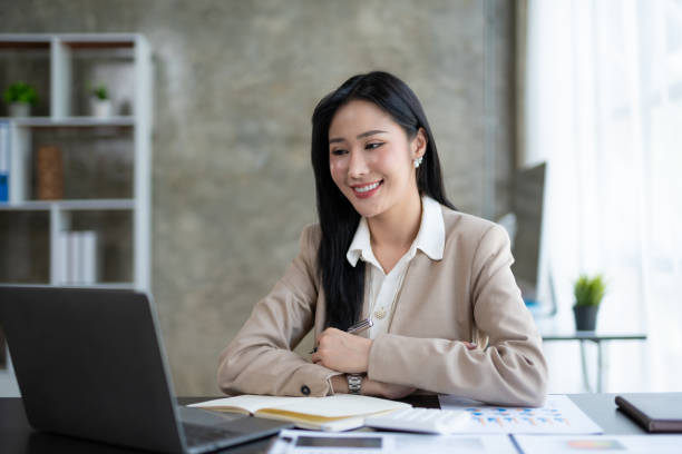 istock Beautiful Asian business woman using her laptop to work and enjoy working, taking note, reviewing assignment and smiling in the office. 2044488829