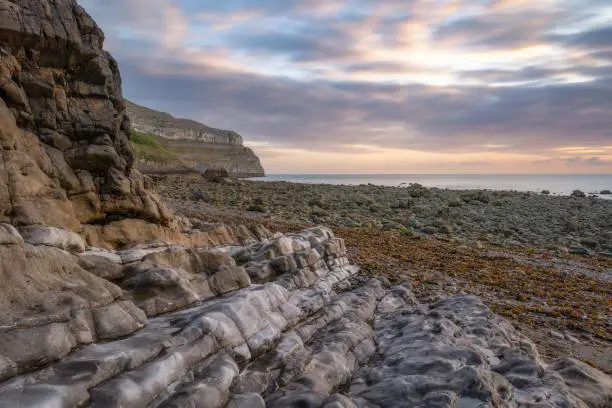 Photo of Sunrise over a rugged rocky coastline with colorful limestone layers - North Wales