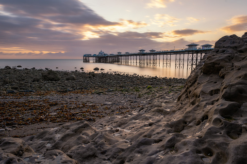 Vibrant colorful sunrise over the rugged rocky coastline with Llandudno Pier in the background - North Wales, United Kingdom