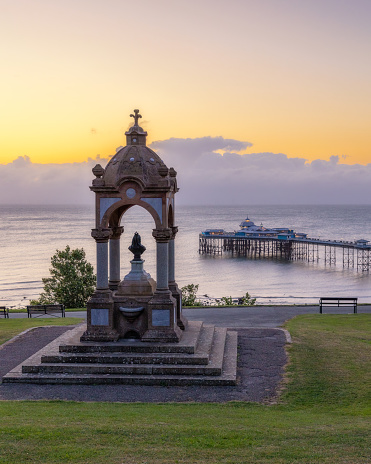 Sunrise glow over the Queen Victoria Memorial and Fountain and Llandudno Pier in North Wales, United Kingdom