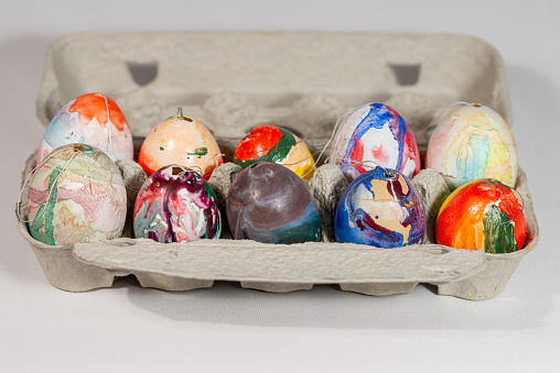 A close-up view of a variety of brightly colored, hand-painted Easter eggs arranged in a paper egg carton