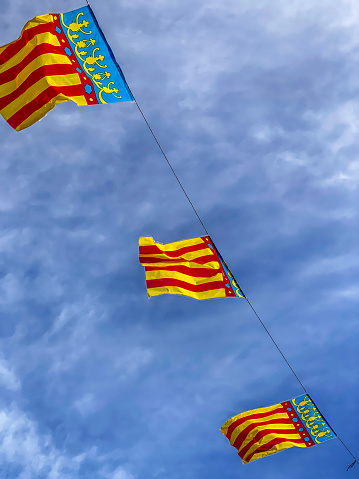 Low angle view of three plastic Valencian flags waving against cloudy sky