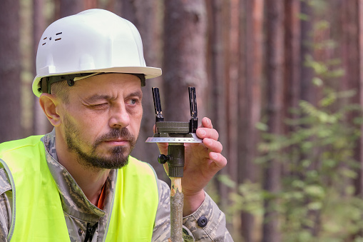 Forest engineer works in the forest with a compass. White helmet and yellow vest. Forestry and forestry. Real people work.