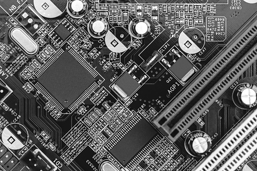 closeup of circuit board with resistors, condensers, microchips and electronic components. b/w.