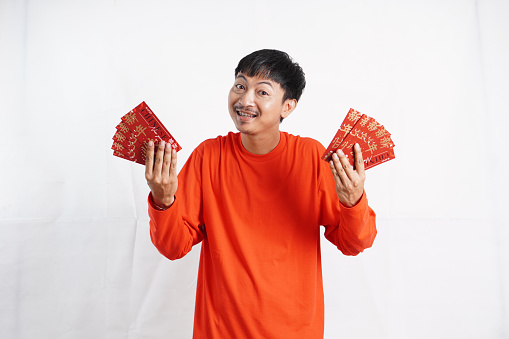 Happy Chinese new year. Asian man holding angpao or red packet monetary gift isolated on white background. Show good luck, greetings, and congratulations. funny face