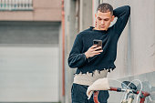 fashionable young man with mobile phone and bicycle in urban background