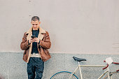fashionable young man with mobile phone and bicycle in urban background