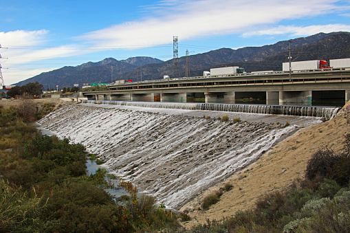 A full flowing San Gabriel River breaking under the concrete 210 Freeway bridge with the lofty San Gabriel Mountains for a background.