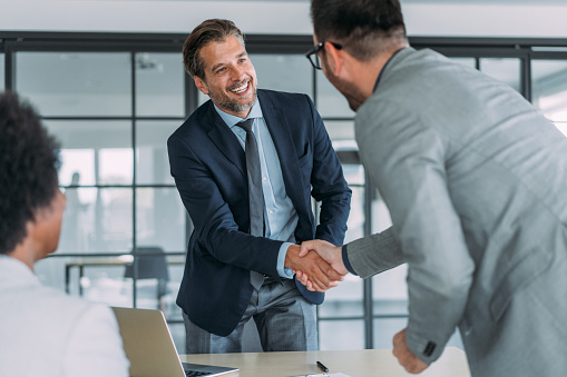 Business people handshaking across the table during a meeting in modern office. Group of business persons in business meeting. Three entrepreneurs on meeting in board room. Corporate business team on meeting in the office.