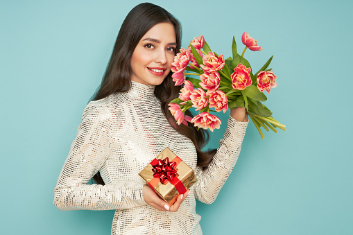 Beautiful young woman hold bouquet of tulips flowers and golden gift box, rejoices spring holiday. Women's Day on March 8th