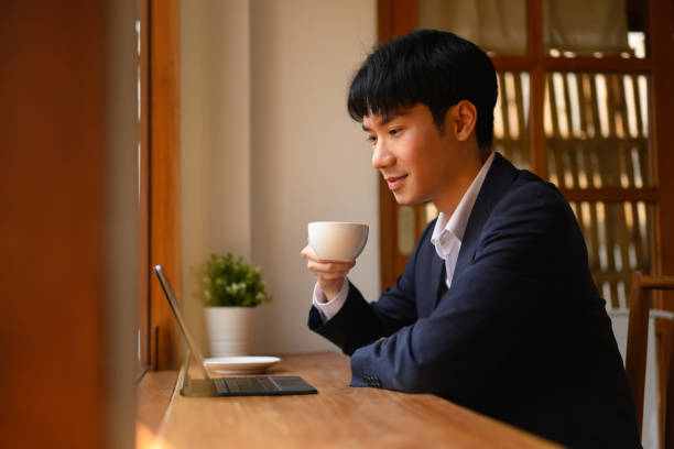istock Handsome young businessman drinking hot coffee and reading email on digital tablet at cafe. 2044773175