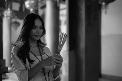 Black and white tone. Beautiful young female tourist holding incense sticks praying at Chinese temple.