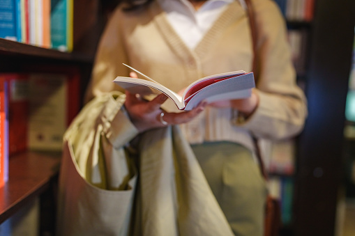 Young woman reading a book in front of a bookshelf in bookstore.