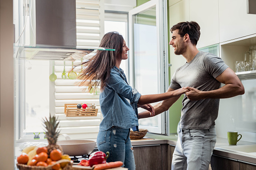 Young happy couple having fun while holding hands and dancing in the kitchen.