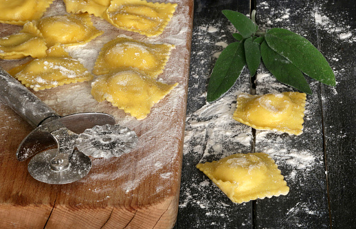 Italian food concept. Homemade ravioli pasta on a floured wooden table and fresh sage. Overhead view.