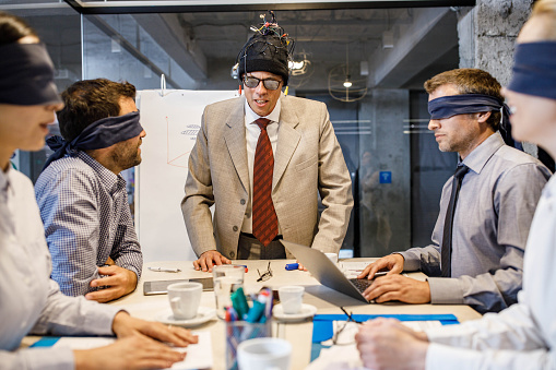 CEO under the influence talking and manipulating with his blindfolded colleagues during a meeting in the office.
