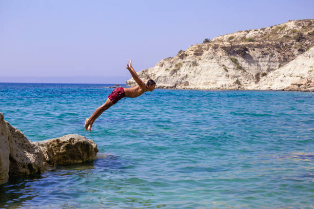istock Young man jumping into the water from the cliff. 2044819427