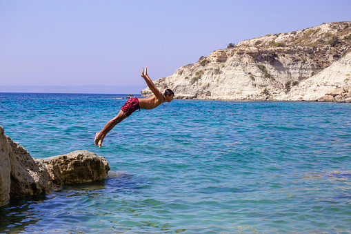 Young man jumping into the water from the cliff.