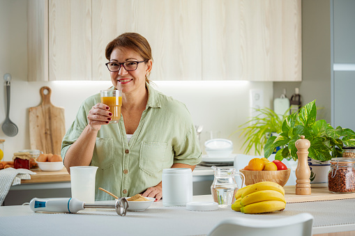 Healthy mature woman drinking nutritional supplement in her kitchen. High resolution 42Mp indoors digital capture taken with SONY A7rII and Zeiss Batis 40mm F2.0 CF lens