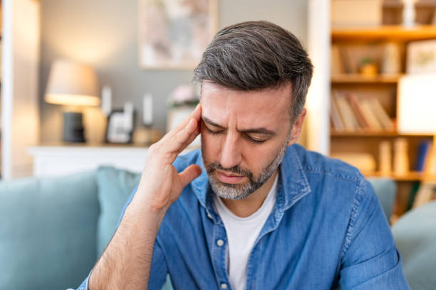 istock Closeup of man suffering from headache at home, touching his temples, copy space, blurred background. Migraine, headache, stress, tension problem, hangover concept 2044859831