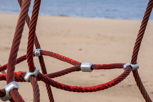 Red rope sections fastened with a metal clamp on a background of brown sand and blue sea