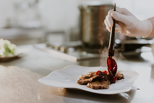 Chef finishing her plate and almost ready to serve at the table. Only hands. Finally dish dressing: steak meat with green salad