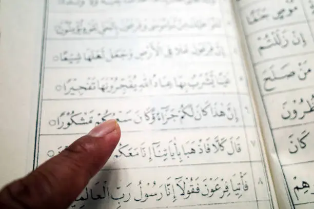 A man fingerpointing to the words in Arabic, in the Qur'an. Learning concept.
