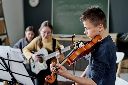 Selective focus shot of modern middle school band practicing music in classroom, copy space