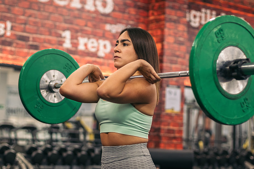 concentrated female athlete lifting barbell during weightlifting workout in gym while looking away