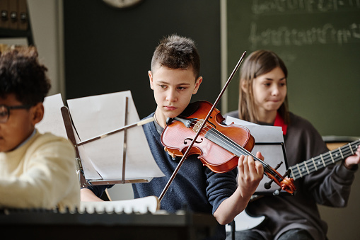Selective focus of boy reading sheet music and playing violin during practice with school orchestra
