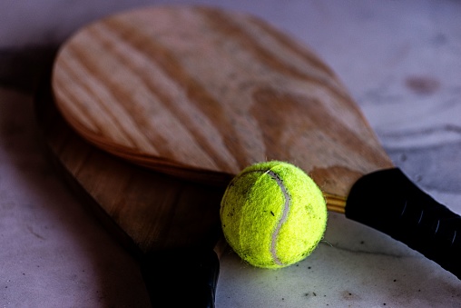 A yellow tennis ball placed on a wooden paddle