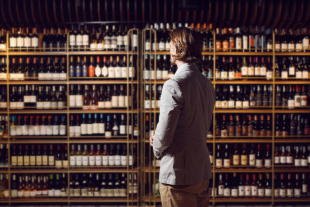 istock Sommelier standing in wine cellar, shelf with many bottles background and looks for necessary alcoholic beverage, make a choise. 2044944219