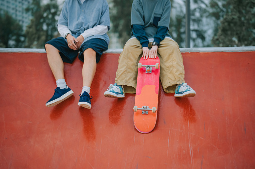 View from below of two young multi-ethnic friends talking and laughing while having fun in a skate park.