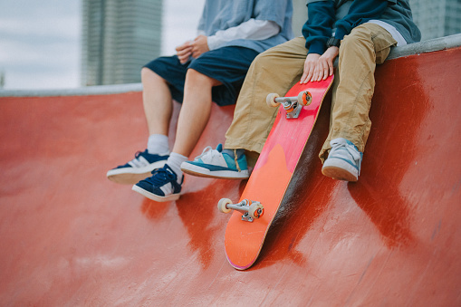 View from below of two young multi-ethnic friends talking and laughing while having fun in a skate park.