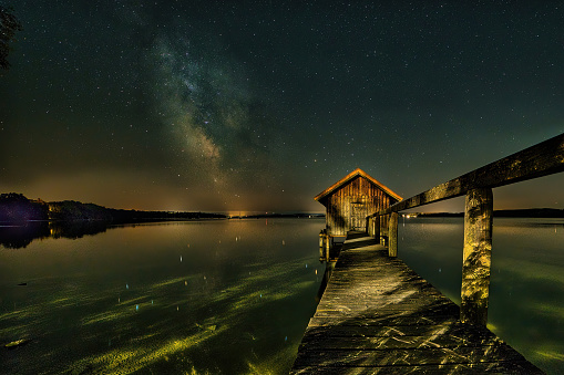 A beautiful milky way sky above a wooden hut over Lake Ammersee, Bavaria, Germany