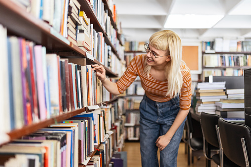 Female student next to bookshelves searching for the book