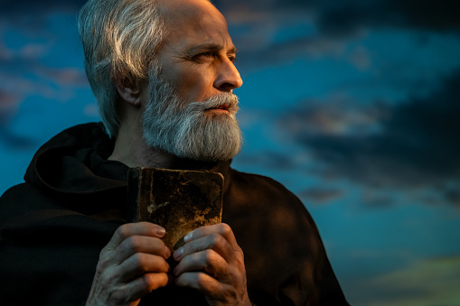 Monk with Holy Bible over dramatic sky