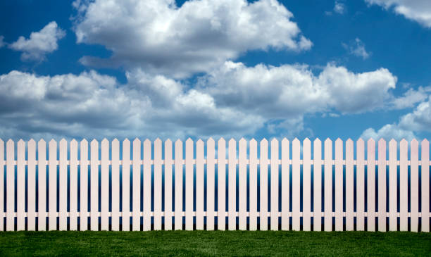 istock White picket fence with green grass and fluffy clouds in the background 2044986894