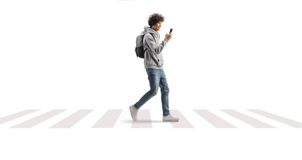 istock Student carrying a backpack and walking at a pedestrian crossing with a smartphone in his hands 2045002520