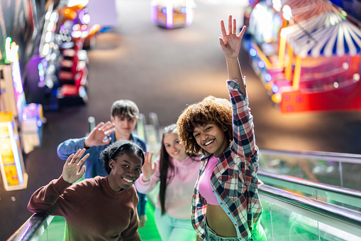 group of young multiracial people on escalators, in games room, partying happily dancing and singing while going up