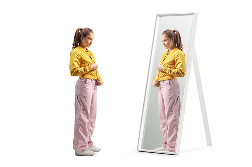 Full length shot of a teenage girl zipping her bomber jacket in front of a mirror isolated on white background