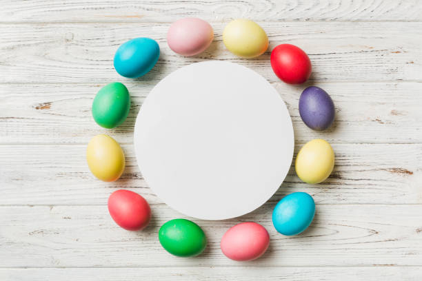 round frame multicolored Easter eggs with white blank paper on a brown background, close-up, space for text, blank for design, selective focus, tinted image.