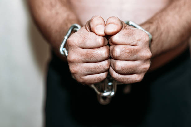 Chained human hands sticking out in a prison.Gray wall.Selective focus.