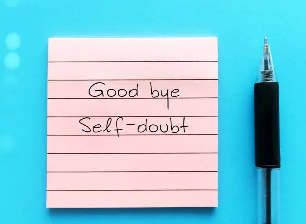 Note on blue background with handwritten text GOOD BYE SELF-DOUBT, concept of overcoming doubting yourself, lack of confidence mindset that holds back from succeeding leads to imposter syndrome or self sabotage
