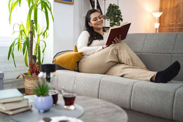 istock Woman reading a book while relaxing on a sofa at home 2045071808