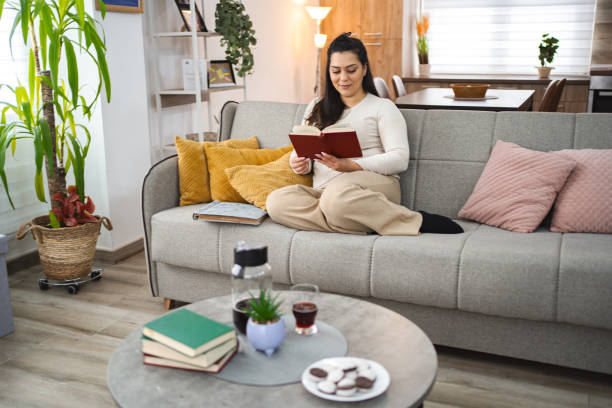 istock Woman reading a book while relaxing on a sofa at home 2045073414